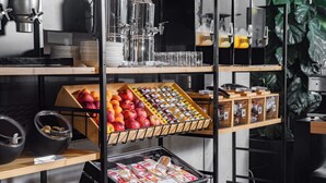 Una barra de desayuno con diversas opciones de comida y bebidas, como frutas, pasteles y máquinas de café.