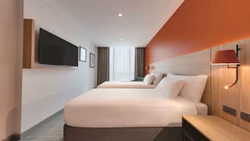 Ein modernes Hotelzimmer mit zwei Betten, einem Flachbildfernseher, einem Nachttisch und einer Lampe.