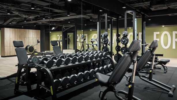 Un gimnasio con equipo de levantamiento de pesas, bancos y un espejo.
