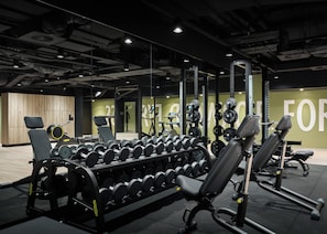 Uma academia com equipamentos de musculação, bancos e espelhos.