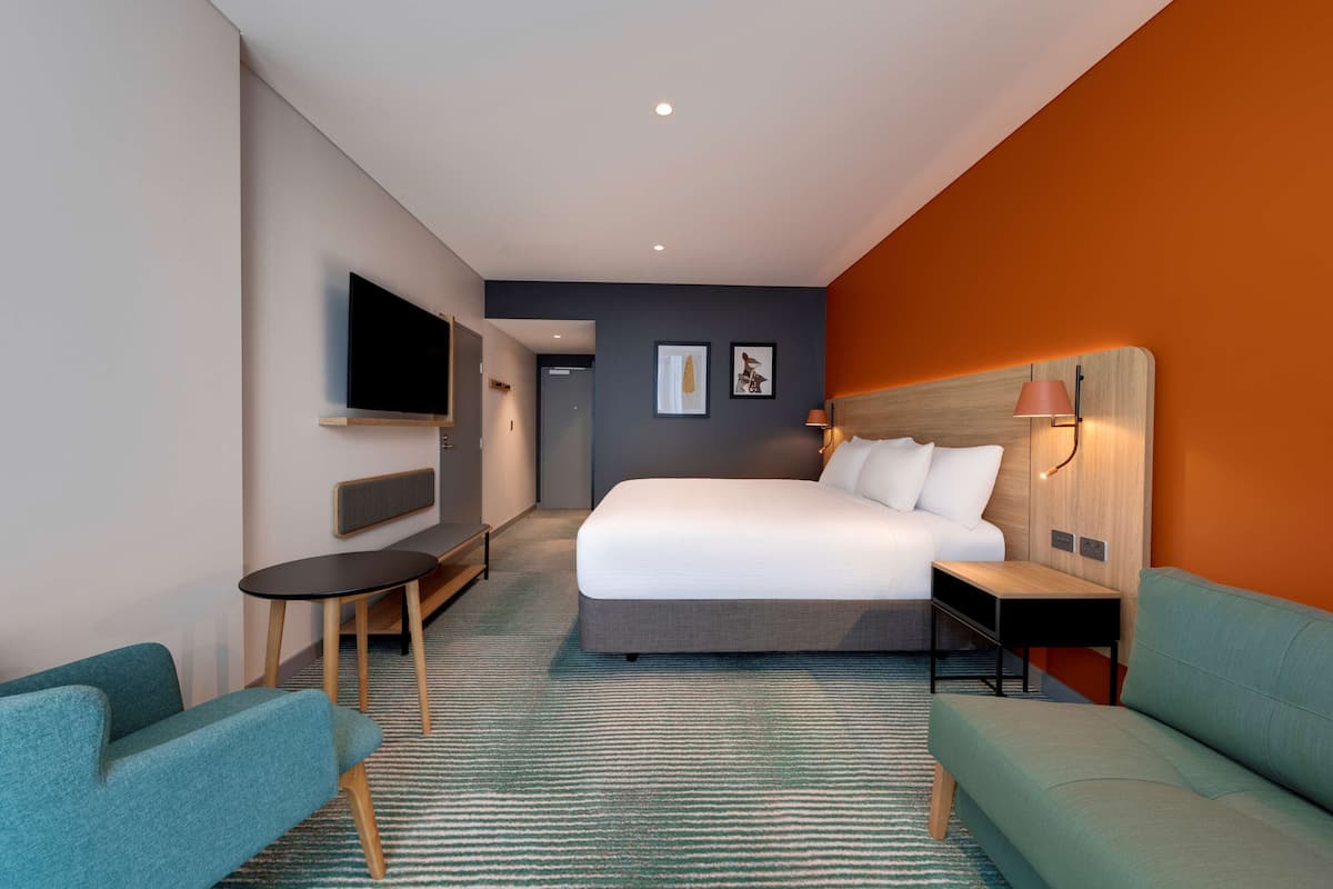 A modern hotel room with a large bed, a TV, a desk, and a sofa.