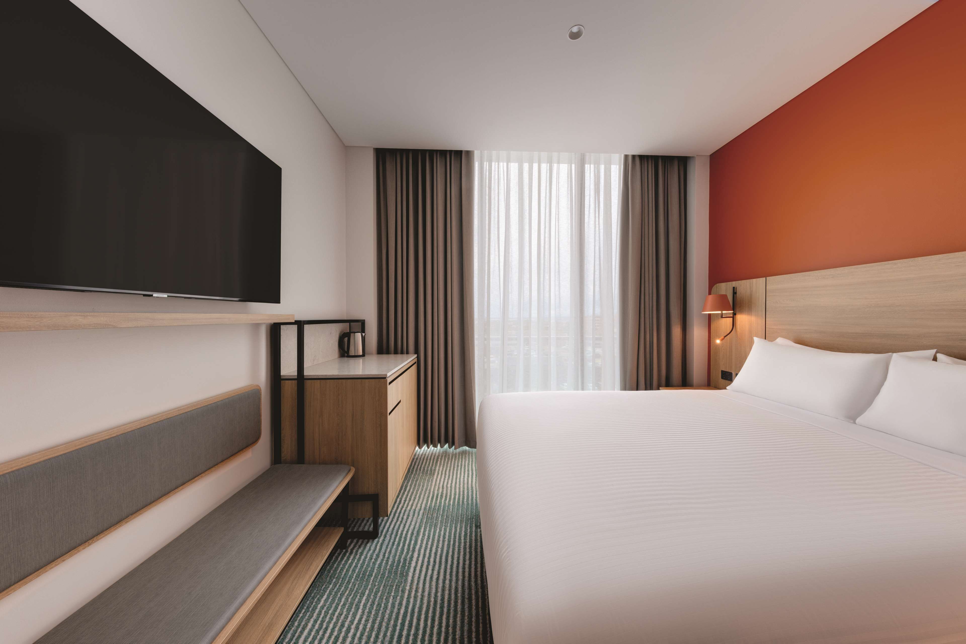 A hotel room with a bed, a desk, a flat-screen TV, a coffee maker, and a window with curtains.