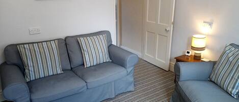 A room with two grey sofas, striped pillows, a striped carpet, a painting on the wall, and a bedside lamp.
