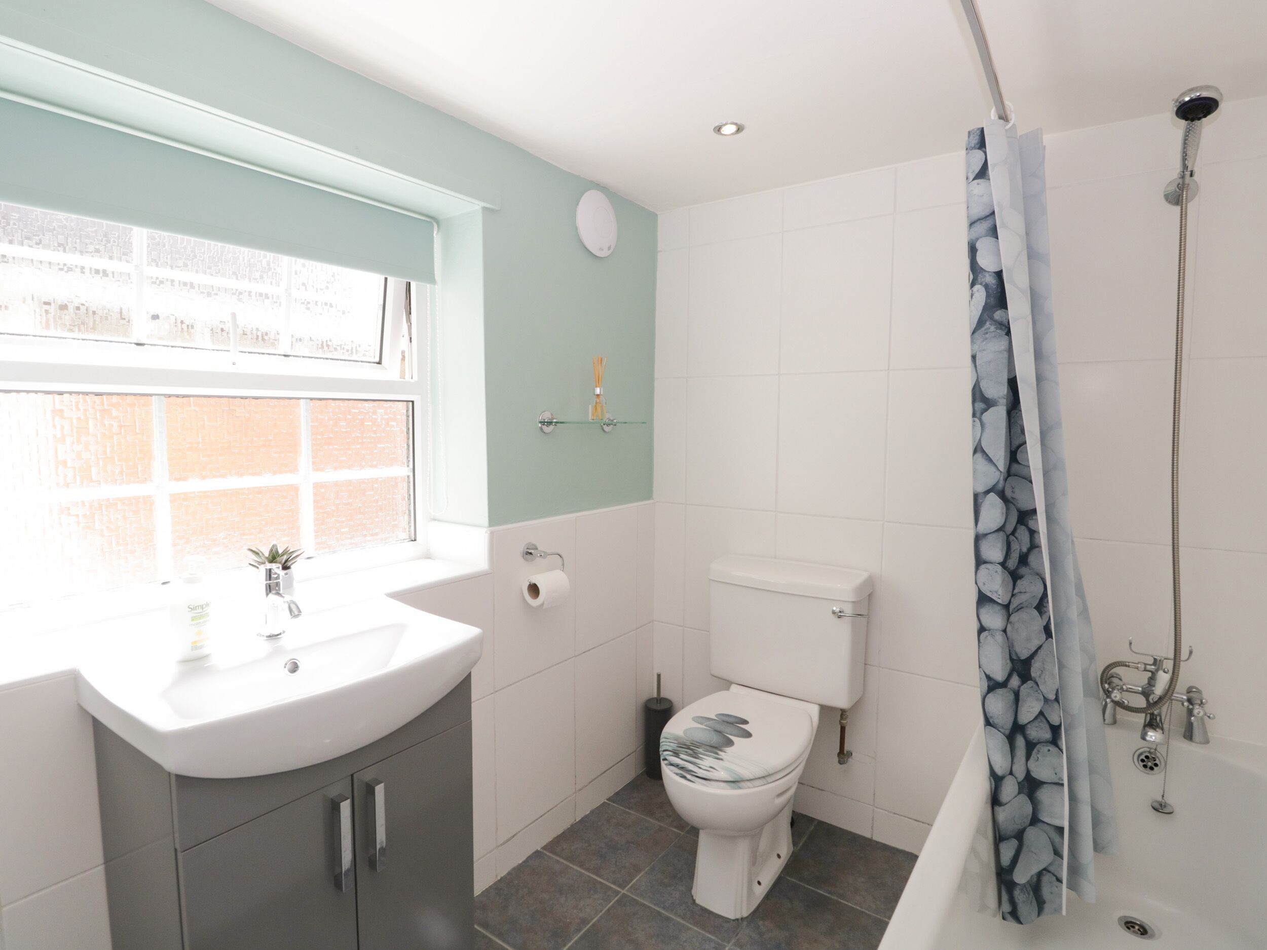 A bathroom with a window, a sink, a toilet, and a shower.