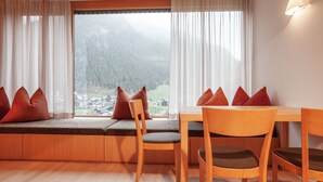 A cozy room with a wooden bench and chairs, a table, and a large window offering a view of a forested area.