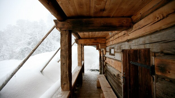 A wooden cabin with a snow-covered exterior and a wooden staircase leading to a bench area.