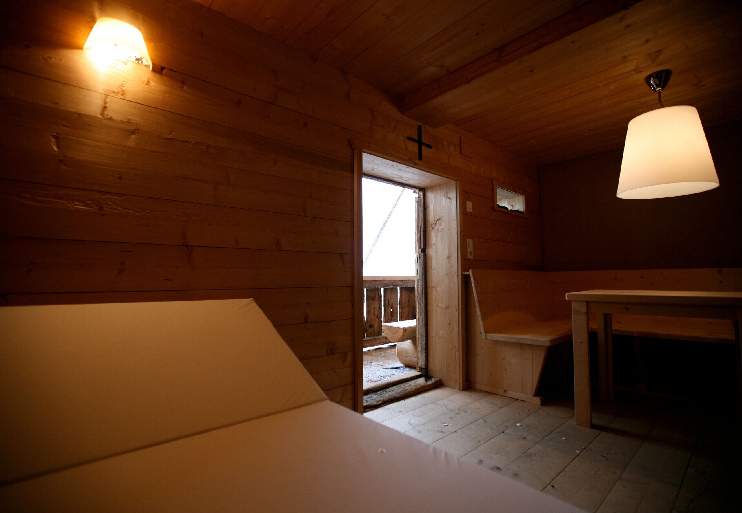 A wooden interior with a door leading outside, a table, and a hanging light fixture.