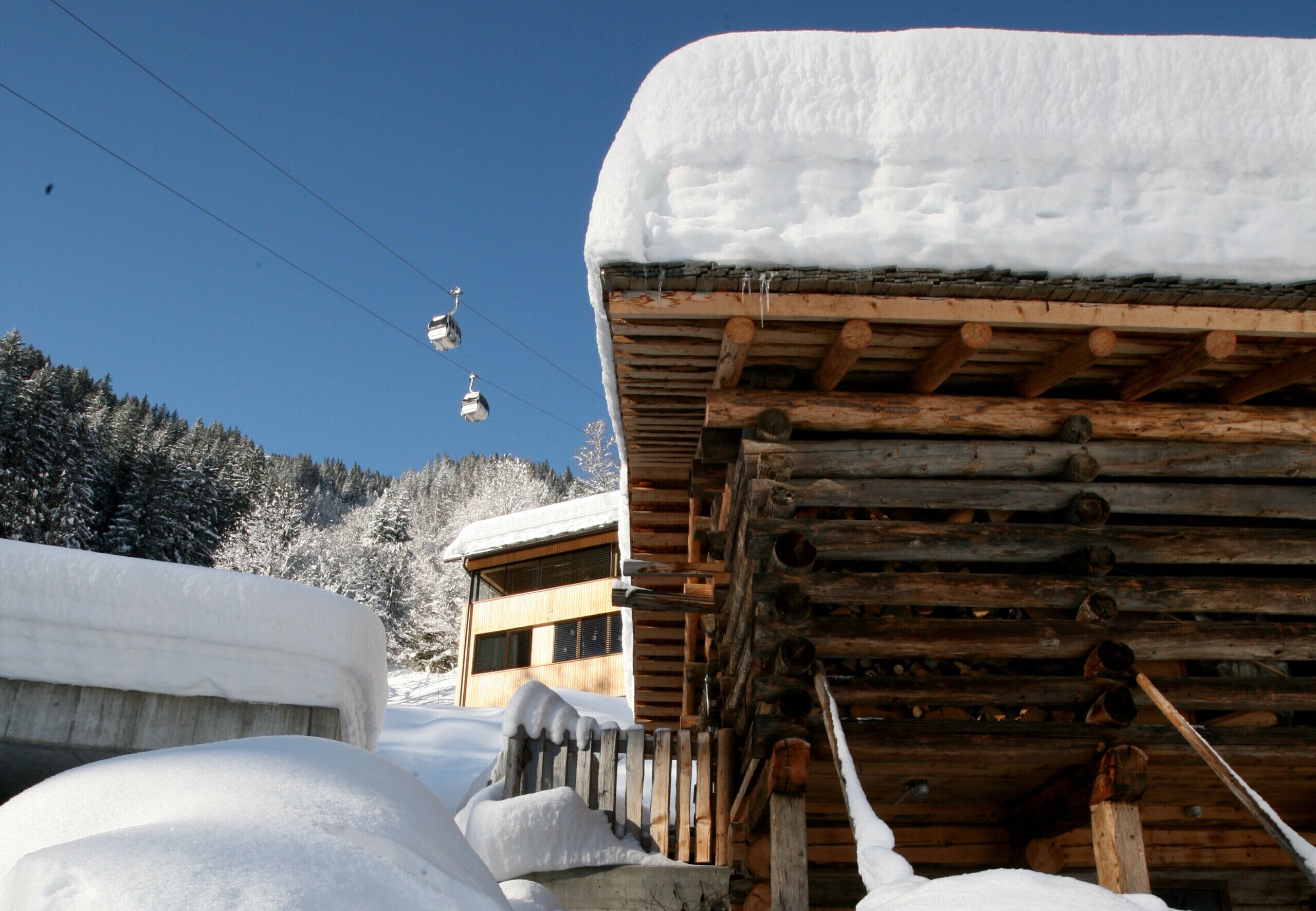 Una cabana de fusta amb un teulat cobert de neu i un teleàsic al fons.