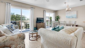 A spacious living room with a ceiling fan, a television, and a dining area with a table and chairs. - 🌴Walk2Beach-Outdoor Patio-3BR Moon Tide Cottage🌴 (Pensacola Beach)