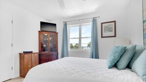 A bedroom with a large bed, a wooden cabinet, a window with curtains, and a ceiling fan. - 🌴Walk2Beach-Outdoor Patio-3BR Moon Tide Cottage🌴 (Pensacola Beach)