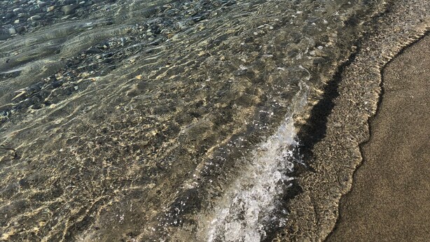 Una platja amb aigua cristal·lina que mostra el fons rocos.