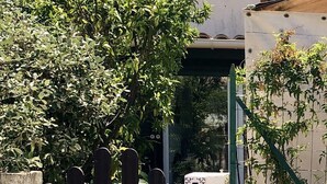 Una porta amb una placa amb un número, una planta en test i un edifici amb teulada i persianes.