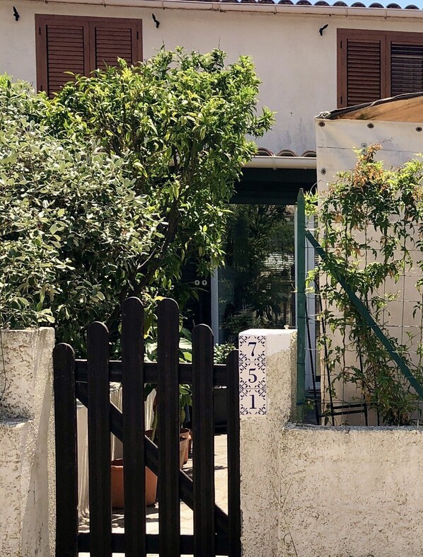 A gate with a number plaque, a potted plant, and a building with a tiled roof and shutters. - La Petite Famille à la mer (Poggio-Mezzana)