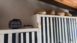 Una habitació amb sostre de fusta, un armari blanc amb tires verticals negres i cistelles teixides a la part superior.