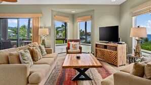 A spacious living room with a large TV, comfortable seating, and a view of the outdoors.