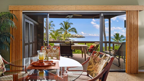 A balcony with a table set for two, overlooking a scenic view of palm trees and a body of water.