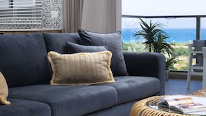 A modern living room with a grey sofa, beige cushions, a woven coffee table, and a view of the ocean. - AmazingApartment W Views of Achziv Beach (Nahariya)