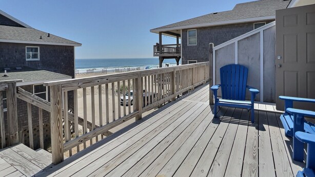 Una terraza de madera con vistas al océano, una silla azul y un edificio con balcón.