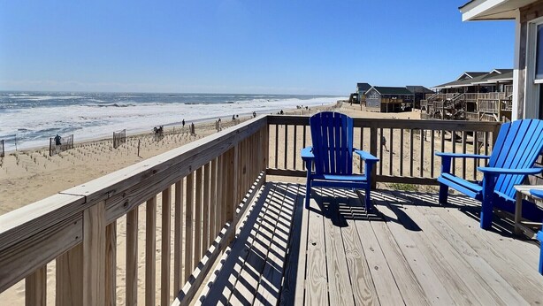 A wooden deck with two blue chairs, overlooking a beach with waves and a clear sky. - Sea Star- Ocean Views- Steps to Beach- Community Pool (Buxton)