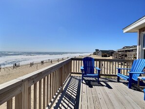 A wooden deck with two blue chairs, overlooking a beach with waves and a clear sky. - Sea Star- Ocean Views- Steps to Beach- Community Pool (Buxton)