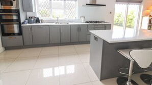 A modern kitchen with grey cabinets, a built-in oven, a gas stove, and a large island with a bar stool. - 17 Clover Hill (Killorglin)