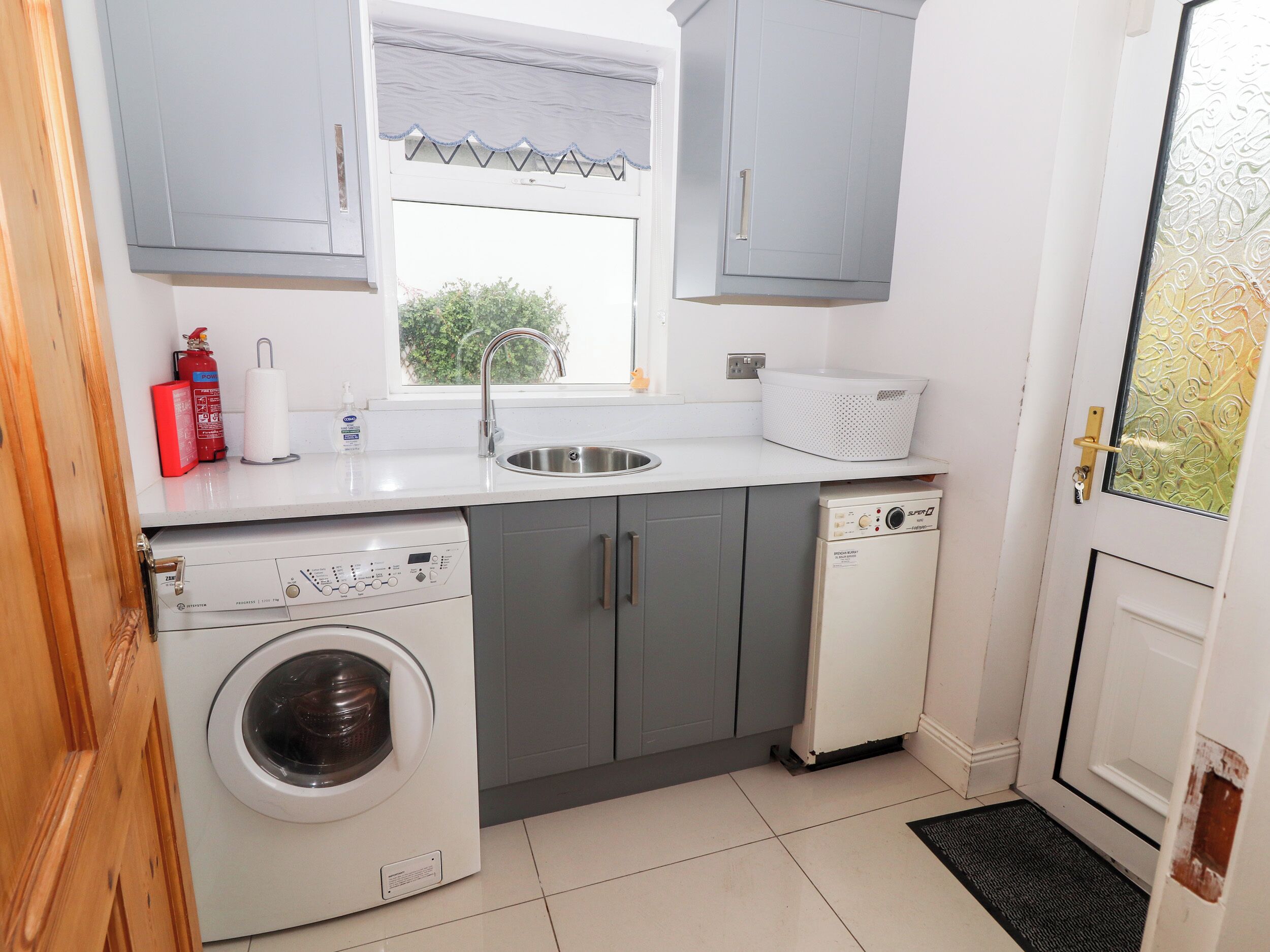 Een kleine keuken met een wasmachine, een vaatwasser, een spoelbak en een raam met uitzicht op groen.