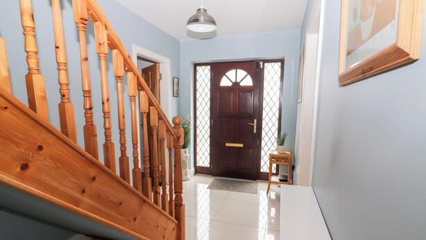 A hallway with a wooden staircase, a door with a window, and a ceiling light. - 17 Clover Hill (Killorglin)