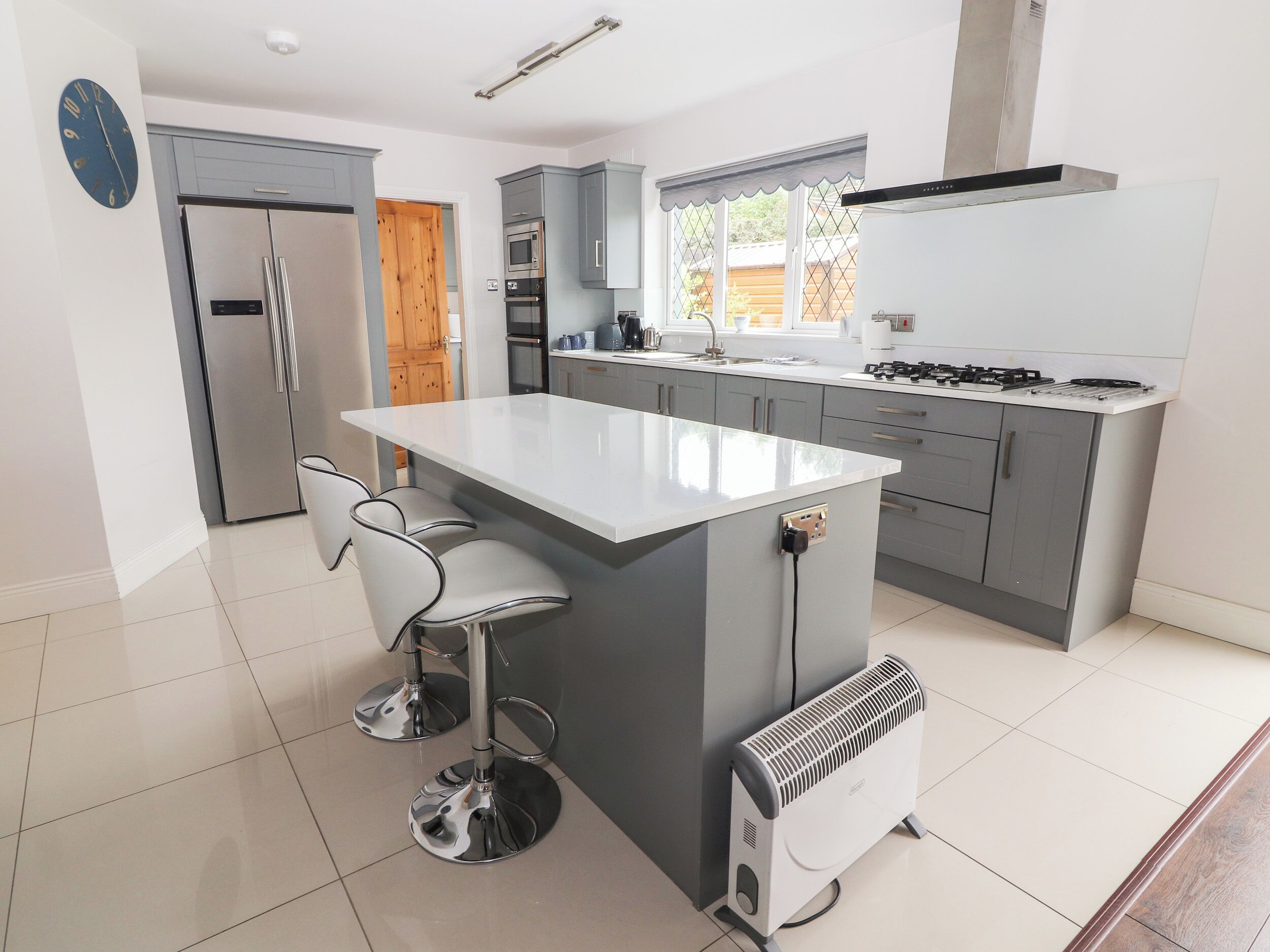 A modern kitchen with grey cabinets, a white island, stainless steel appliances, and a built-in oven.