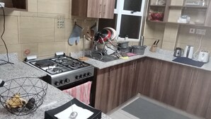 A kitchen with a gas stove, wooden cabinets, a window, and various kitchen utensils. - perfect apartment (Nairobi)