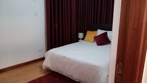 A bedroom with a bed, a red rug, a white wall, and a dark curtain. - perfect apartment (Nairobi)