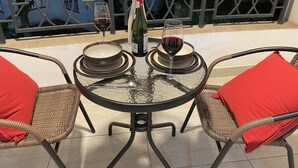 A round glass table with two plates, two glasses of red wine, and a bottle of wine. There are wicker chairs with red cushions. - perfect apartment (Nairobi)