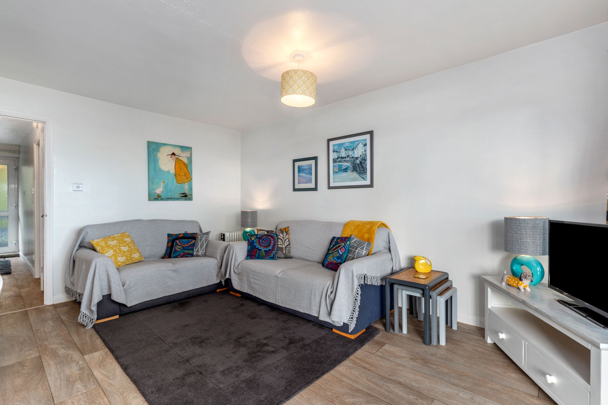 A modern living room with a grey sofa set, a small coffee table, a TV stand, and two framed pictures on the wall.