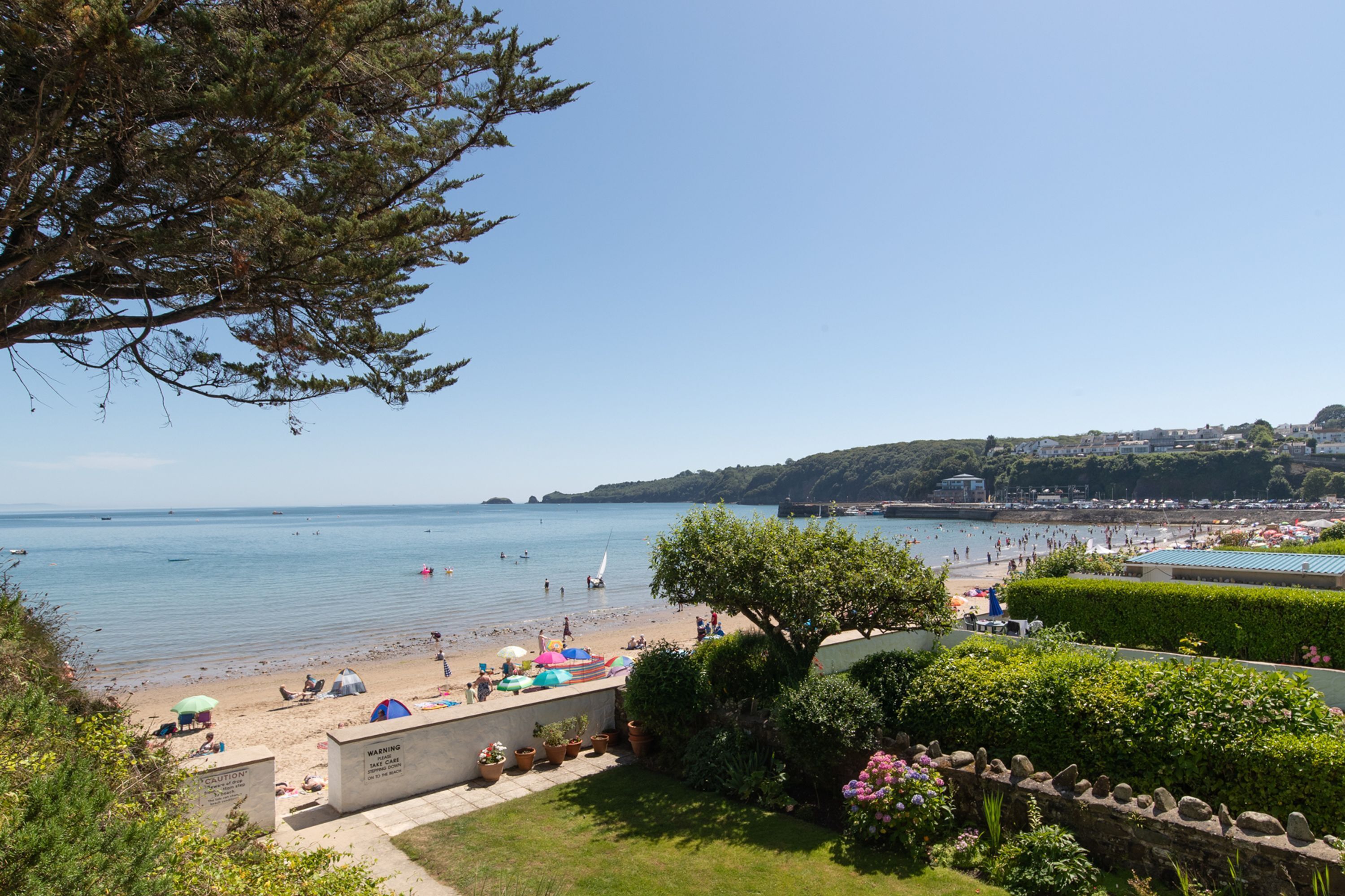 Une plage avec des parasols, des gens et un voilier.