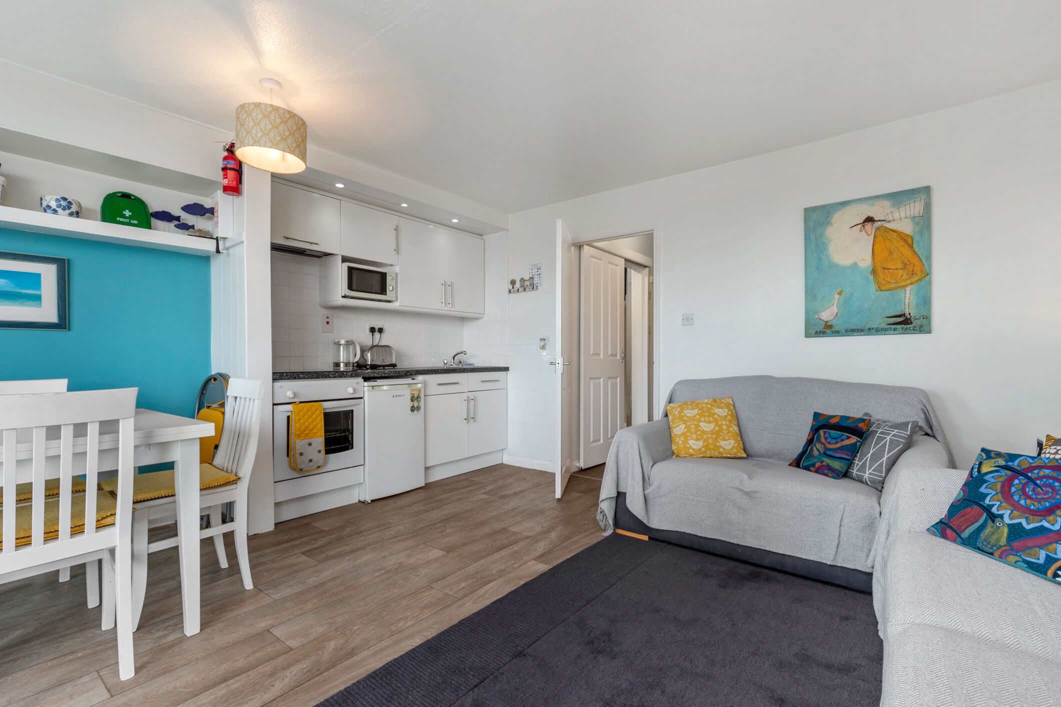 A compact living space with a kitchenette, a dining area, and a sofa with colorful cushions.
