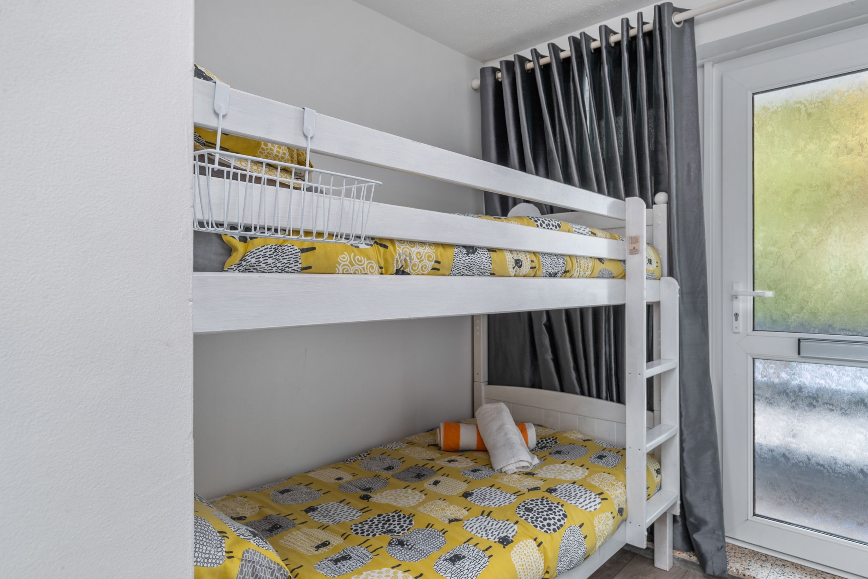 A bunk bed with a white frame, a yellow patterned bedspread, and a white headboard.