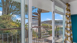 Ein Balkon mit Glastür, die zu einer Wendeltreppe führt, Blick auf eine Hügelterrasse und ein Blumentopf.