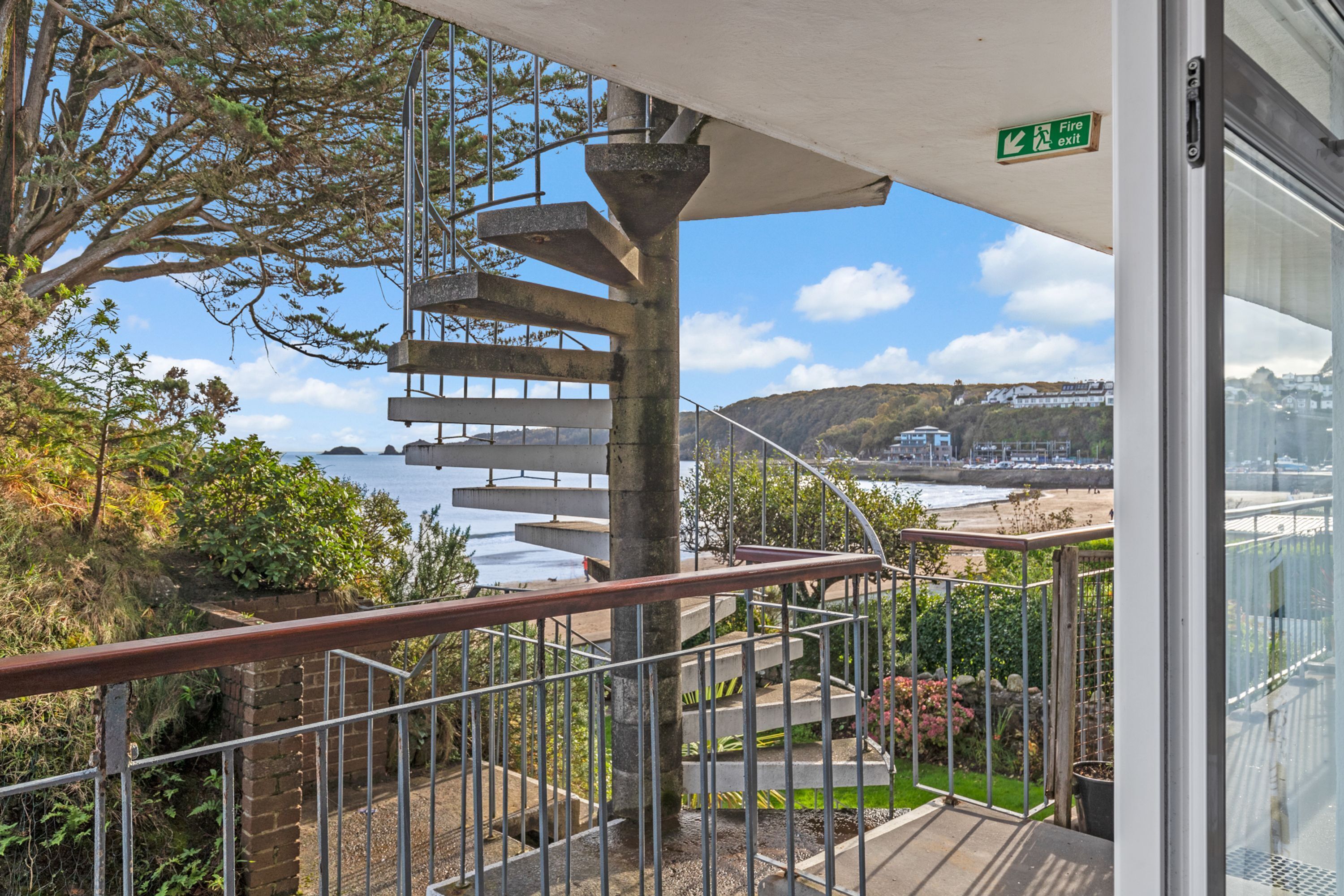 A spiral staircase leading to a balcony overlooking a coastal area with a view of the sea and hills.