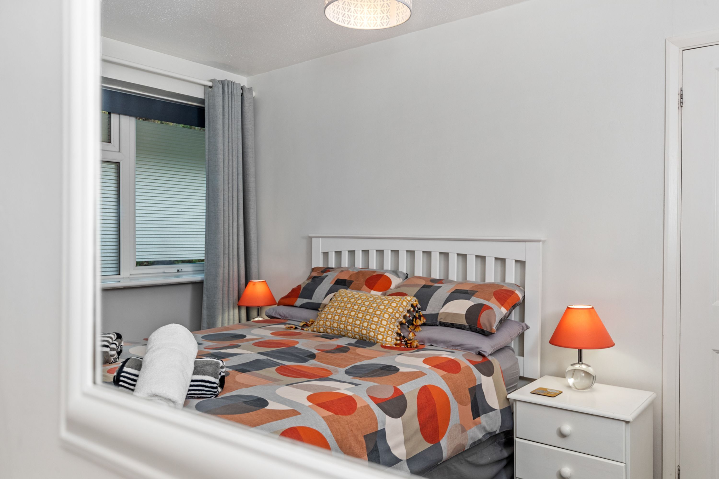 A neatly arranged bedroom with a bed, two bedside tables, a window with curtains, and a nightstand with a lamp.