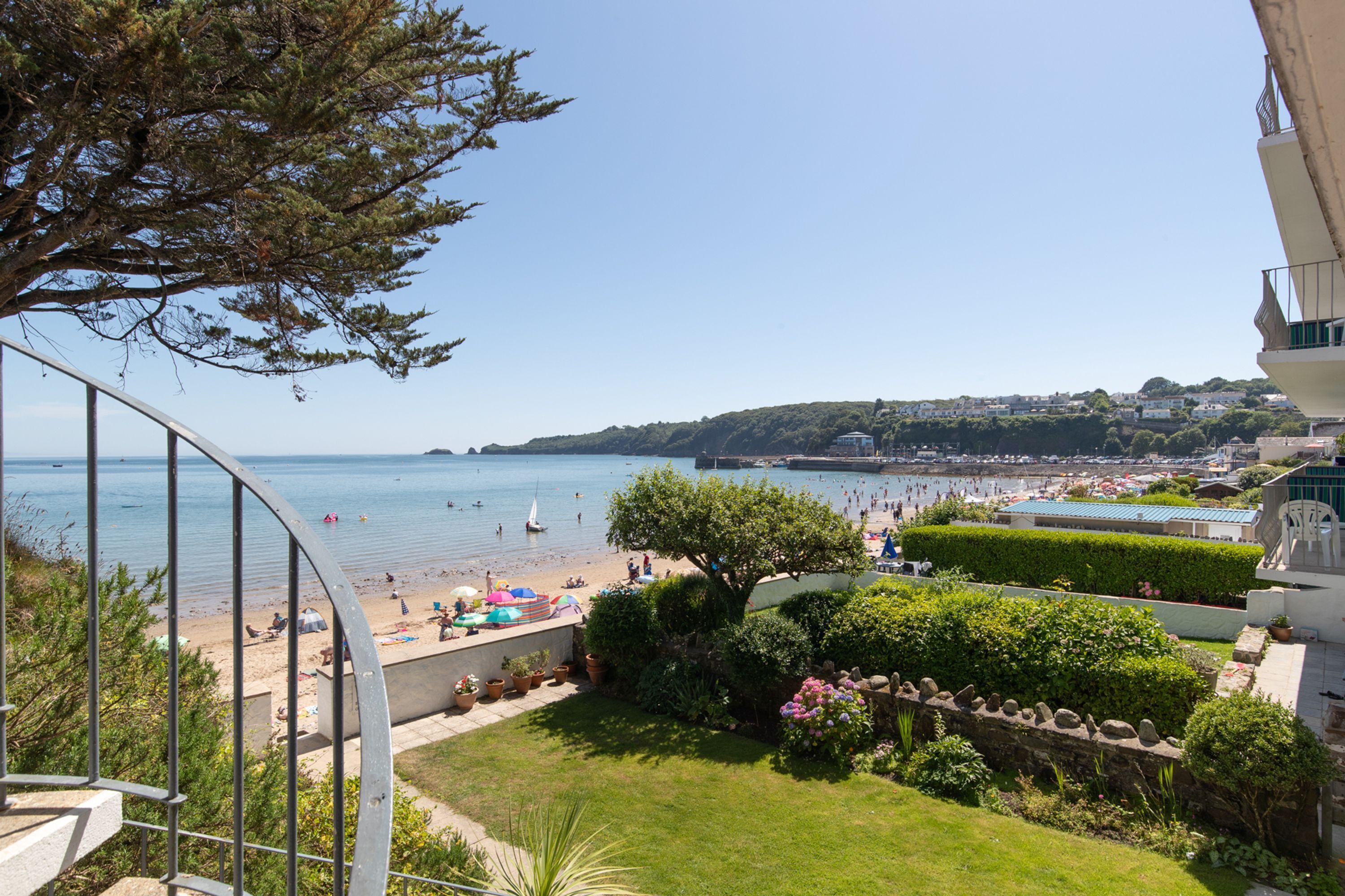 A coastal view from a balcony overlooking a beach with people and boats.