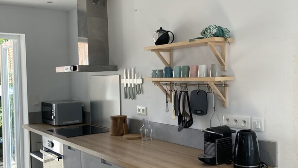 Cozinha moderna com bancada de madeira, eletrodomésticos de aço inoxidável e forno embutido. Utensílios pendurados e uma cafeteira na parede.