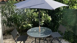 Uma mesa de vidro redonda com quatro cadeiras, um guarda-sol e uma janela pequena.