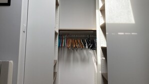 Um closet amplo com espaço para pendurar roupas e prateleiras, um interruptor de luz e um termostato na parede.