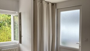 Quarto com radiador, janela com cortina e porta de vidro jateado.