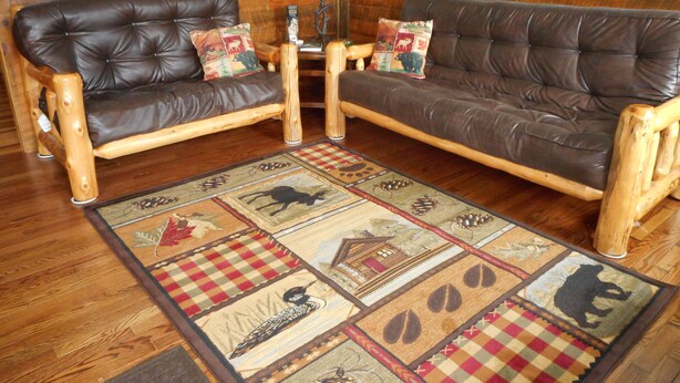 A living room with two leather sofas, wooden armchairs, a patterned rug, and a wooden floor. - Post and beam cabin with queen size  and bunk (Shirley Mills)