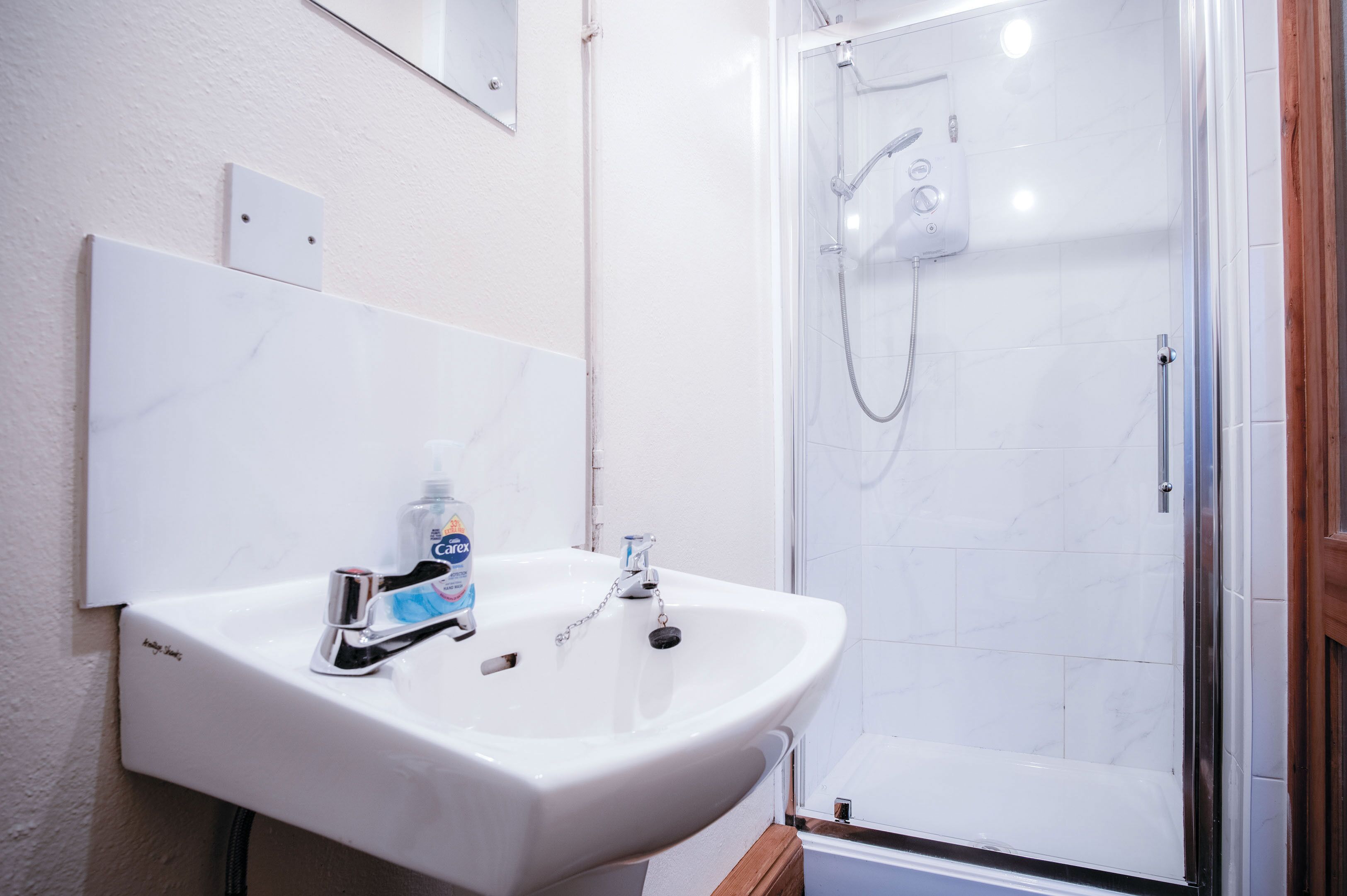 Ein Badezimmer mit einem weißen Waschbecken, einem Spiegel und einer Duschkabine.