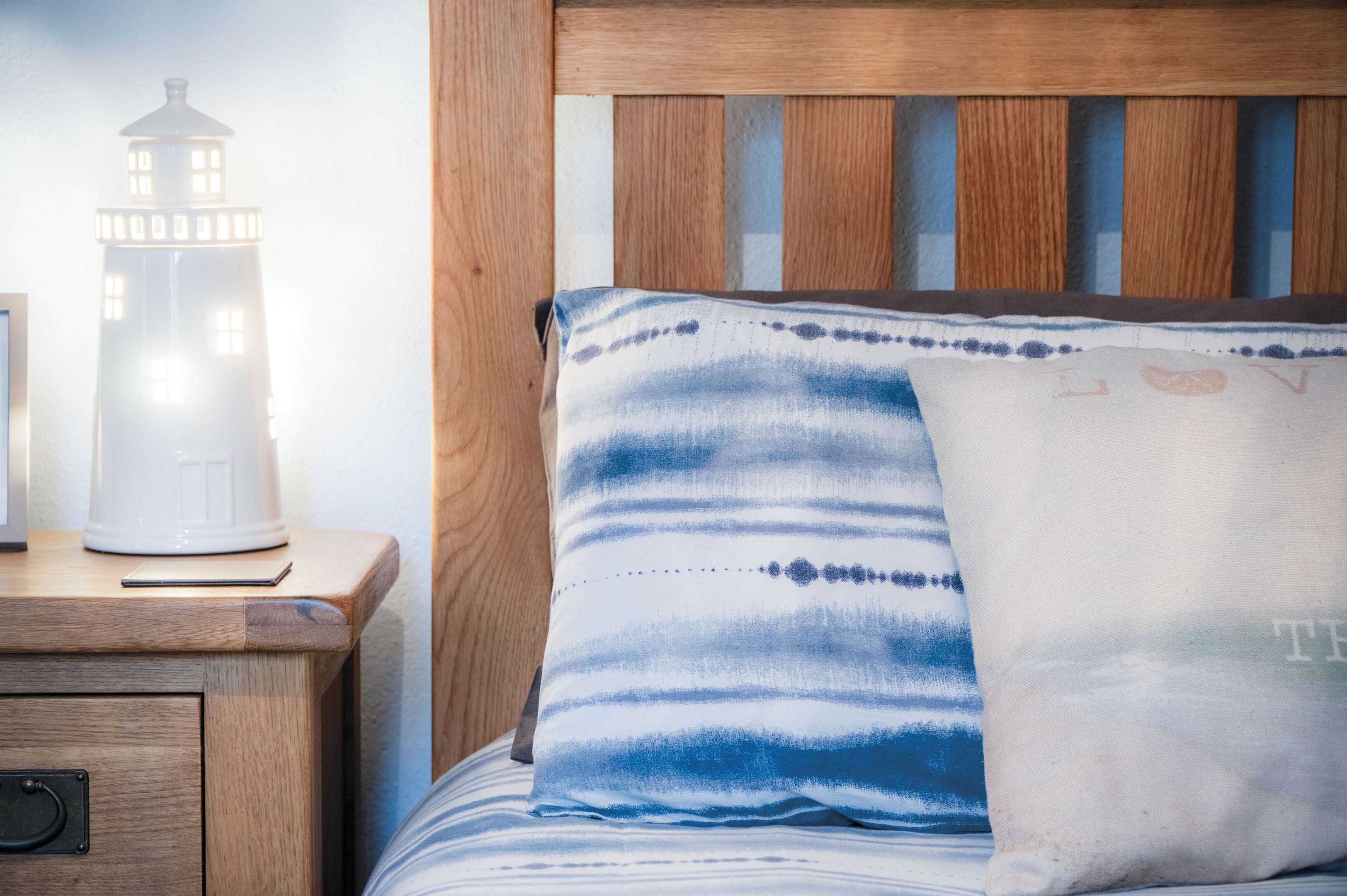 A wooden bedside table with a white lamp and a bed with blue and white patterned bedding.