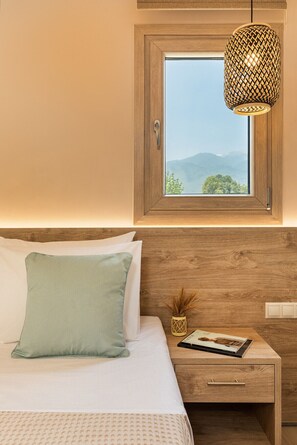 A bedroom with a wooden headboard, a window with a view of mountains, a bedside table with a lamp, and a bed with pillows. - Makris Luxury Rooms (Dio-Olympos)