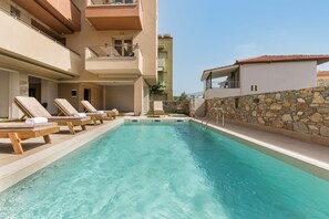 A swimming pool with lounge chairs and a stone wall. - Makris Luxury Rooms (Dio-Olympos)