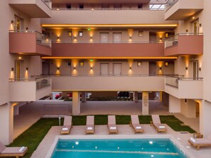 A multi-story hotel with a pool area, outdoor seating, and a well-lit balcony. - Makris Luxury Rooms (Dio-Olympos)