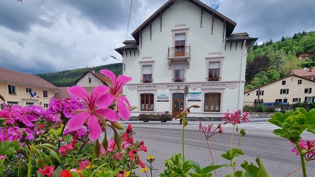 Ein zweistöckiges Gebäude mit Balkon, einem Schild für 'AGENCE IMMOBILIER' und einem Schild mit 'MEUBLES TOURISTIQUES'.